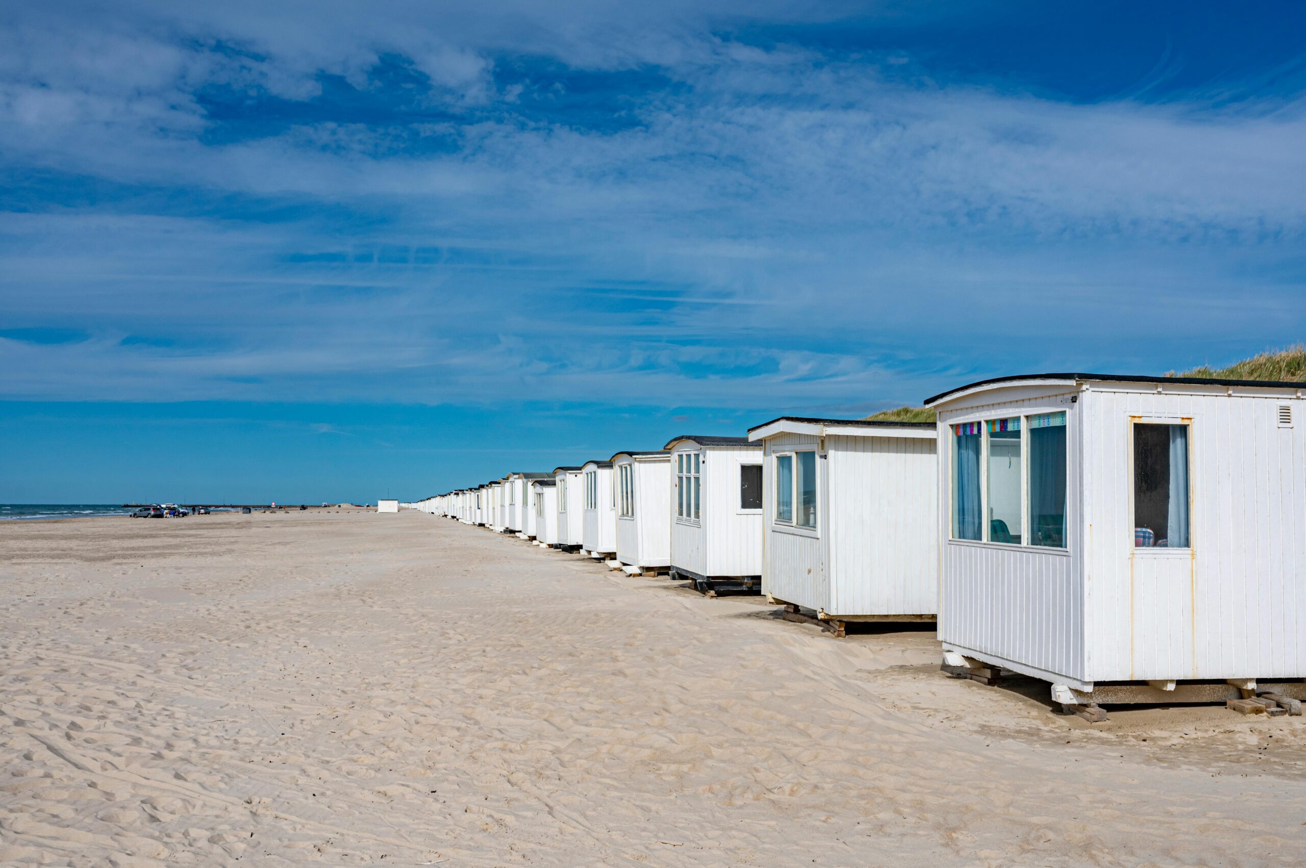 A row of white beach cabins along the sandy coast of Løkken, Denmark.